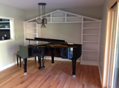 image shows a grand piano in a room with hardwood floors, light-colored walls, and a vaulted ceiling