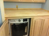 image shows a washing machine installed inside a wooden cabinet.