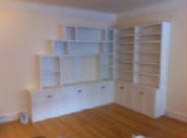 image shows a corner of a room with built-in white bookshelves and cabinets